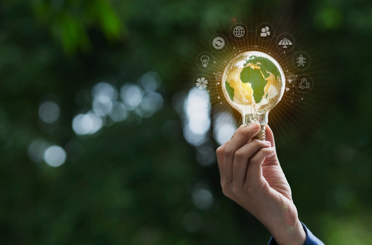 hand holding light bulb with sustainability icons on green background with technology and environment concept