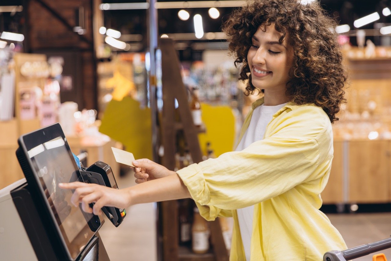 young woman in a yellow shirt using a self check out POS at a supermarket